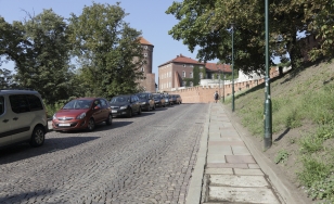 stromy podjazd pod górę, nierówna kostka brukowa na jezdni, nierówne płyty chodnikowe z wysokim progiem, wzdłuż drogi po lewej stronie stoją samochody