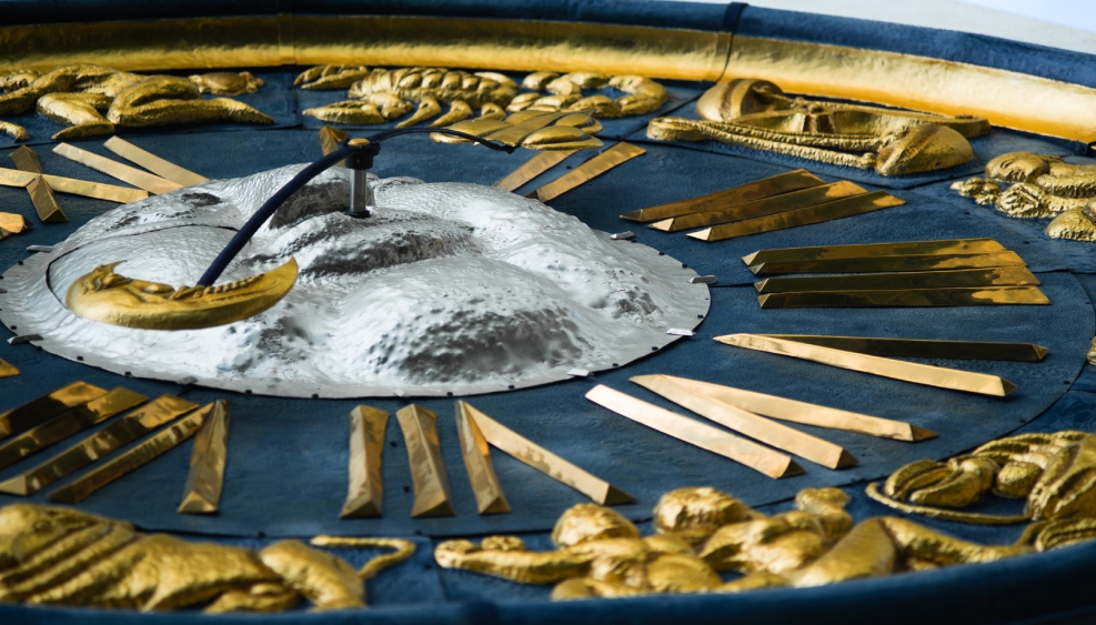 fragment dużego zegara, niebieska tarcza i złocone wskazówki i oznaczenia godzin